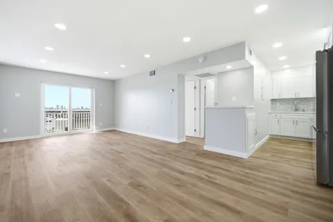 a view of an empty room with wooden floor and a kitchen