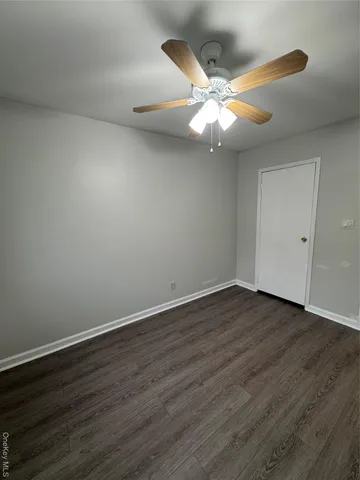 a view of an empty room with wooden floor and a ceiling fan