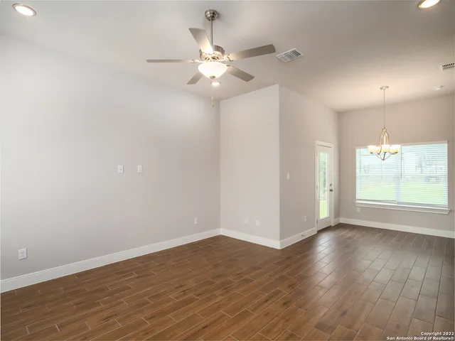 an empty room with wooden floor fan and windows