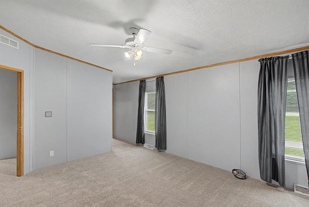 1202 Princeton Road Princeton, LA 71067 - Photo 14 of 19 Spacious interior room featuring light grey paneled walls with wood-finish trim, neutral carpet flooring, and a ceiling fan with integrated lighting