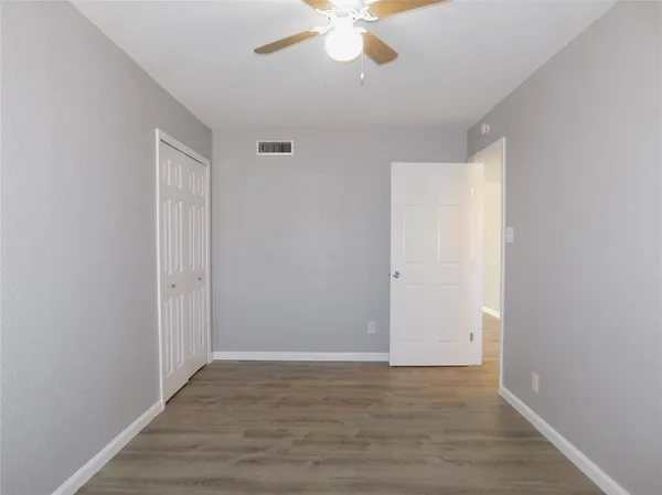 a view of an empty room with wooden floor and a ceiling fan