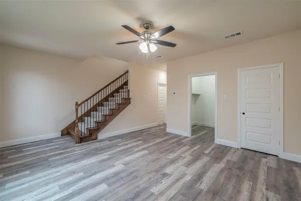 a view of an empty room with wooden floor and a ceiling fan