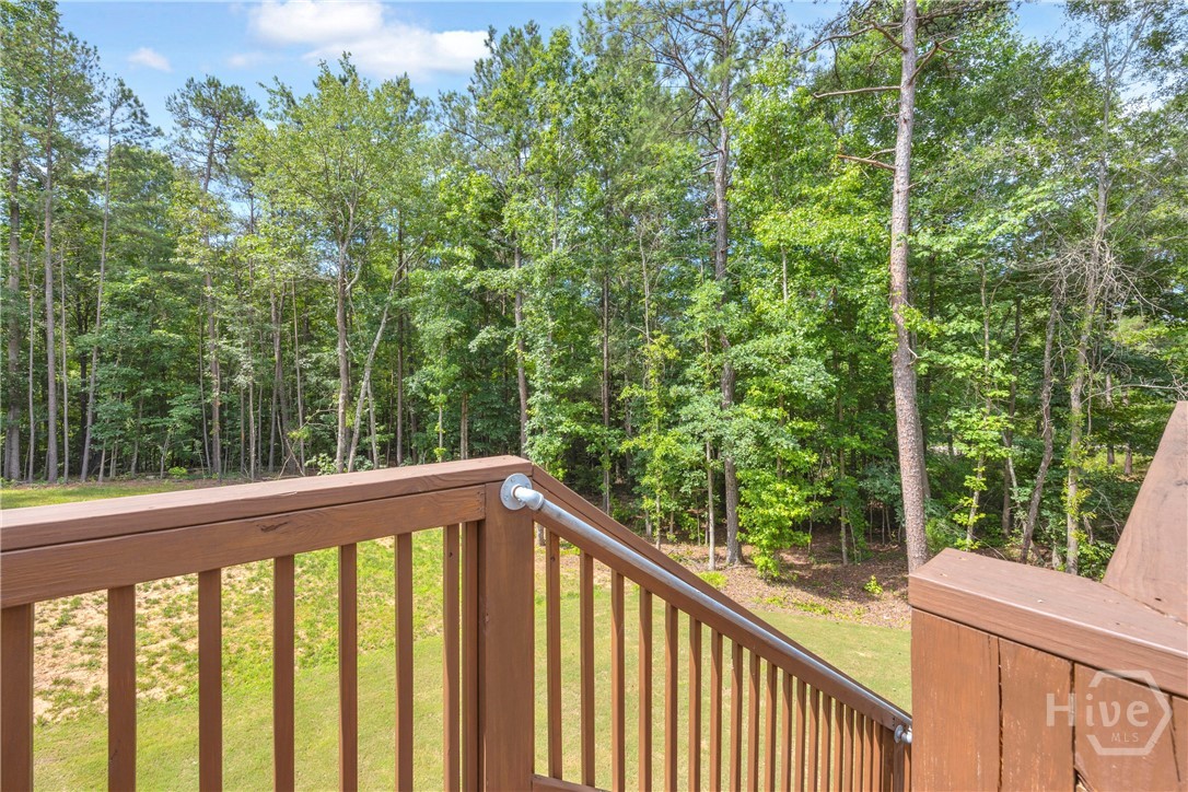 2476 St Martin Way Monroe, GA 30656 - Photo 66 of 75 Wood-toned deck railing with a metal handrail overlooking a sloped grassy area and extensive tree line