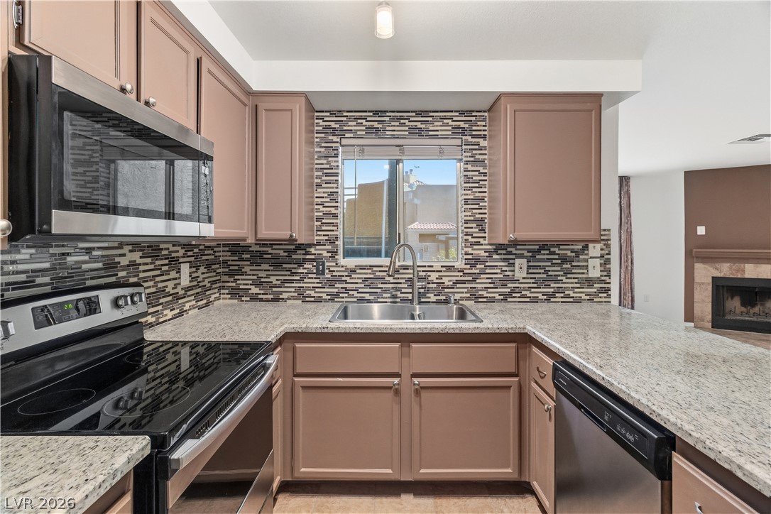 2232 Aspen Mirror Way, Unit 103 Laughlin, NV 89029 - Photo 12 of 50 Kitchen featuring stainless steel appliances, a tiled fireplace, light stone counters, decorative backsplash, and a peninsula