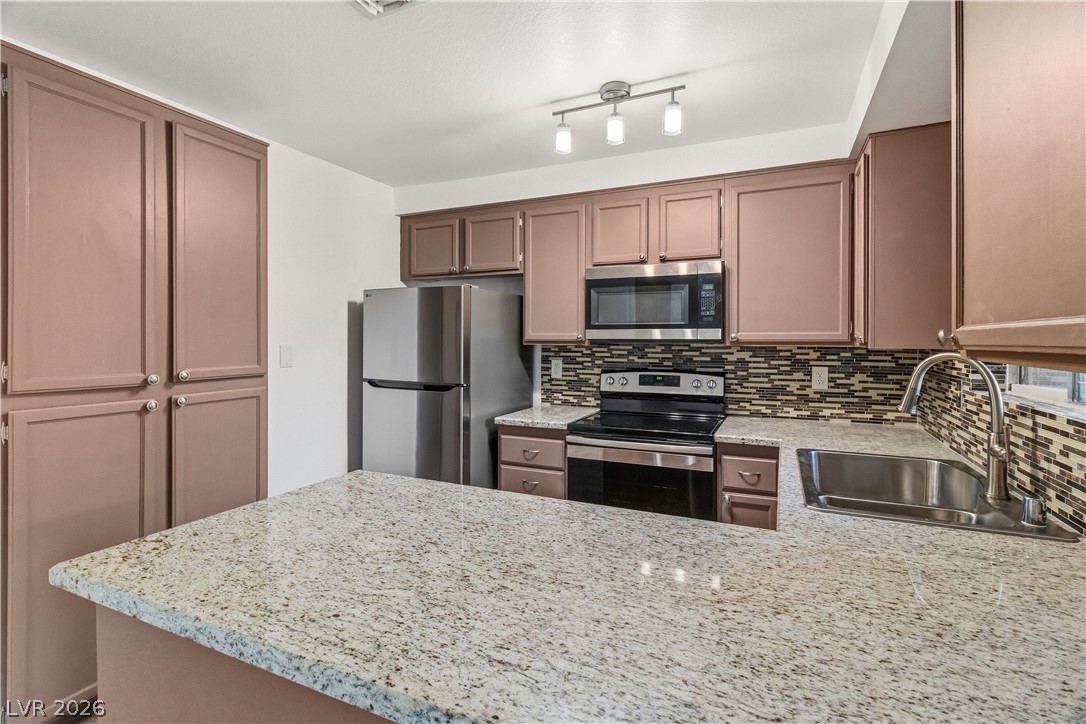 2232 Aspen Mirror Way, Unit 103 Laughlin, NV 89029 - Photo 9 of 50 Kitchen featuring stainless steel appliances, a peninsula, decorative backsplash, and light stone countertops