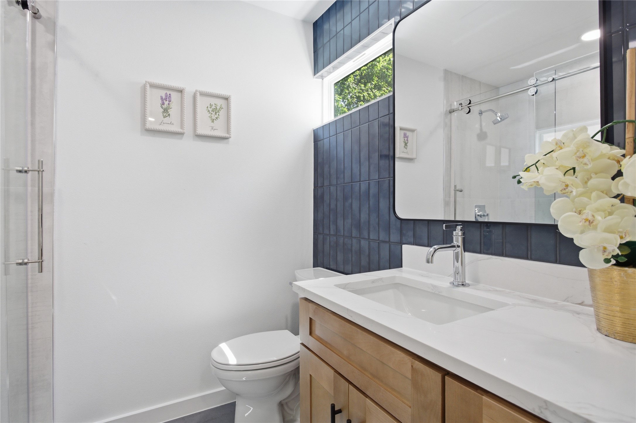 2110 Magazine Street Austin, TX 78727 - Photo 19 of 31 Bathroom featuring a wood-finish vanity with a single basin sink and light-toned countertop, a rectangular mirror, and a window above a dark tile accent wall