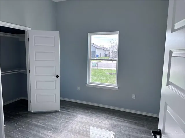an empty room with wooden floor closet and windows