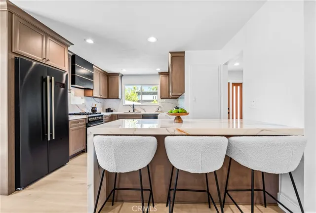 a kitchen with stainless steel appliances granite countertop a dining table chairs refrigerator and sink