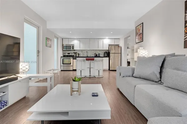 a living room with stainless steel appliances furniture a rug and a kitchen view