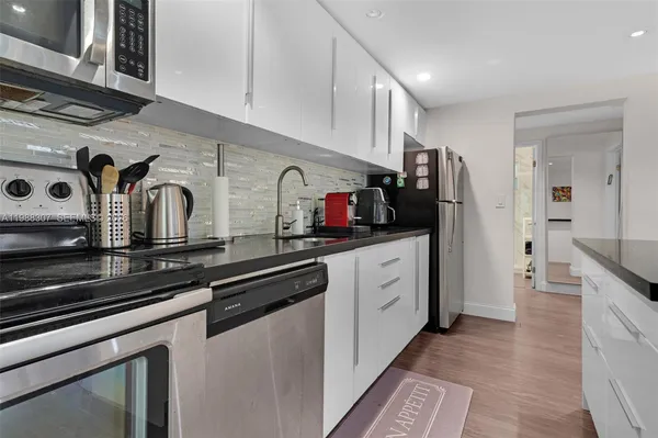 a kitchen with stainless steel appliances granite countertop a refrigerator a stove a sink and white cabinets with wooden floor