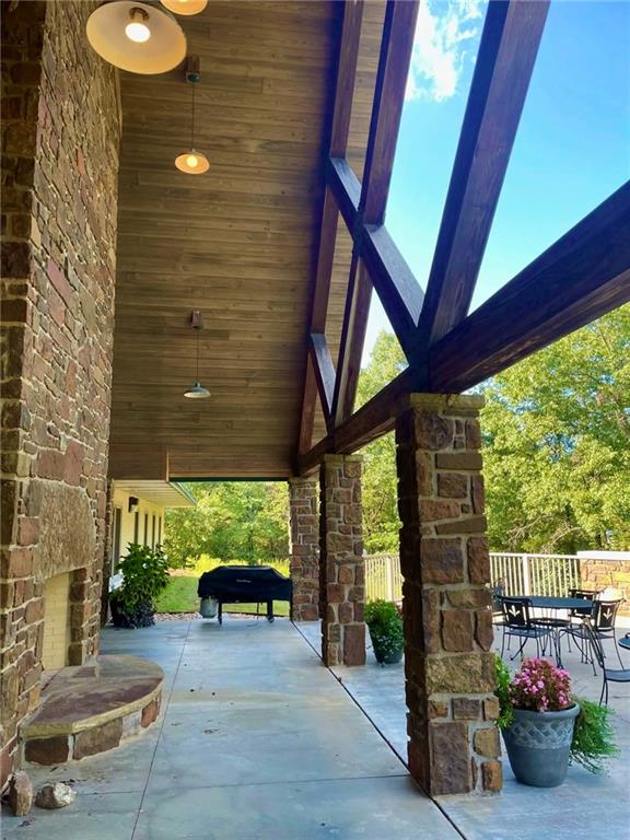8524 Youth Ranch Road Mulberry, AR 72947 - Photo 18 of 40 Covered stone patio featuring a plank wood ceiling, exposed wood beams, stone columns, and an outdoor stone fireplace