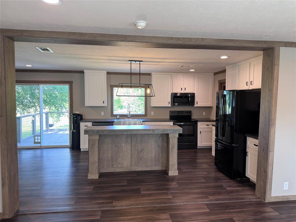 7268 Brangus Road Anna, TX 75409 - Photo 9 of 21 Kitchen featuring a central island with a wood-finish base and light-colored countertop, white cabinetry with black hardware, black appliances, and wood-finish flooring