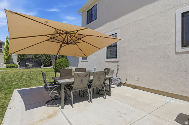 10676 Urban Rdg Cove South Jordan, UT 84095 - Photo 44 of 48 Concrete patio featuring a large rectangular umbrella, stucco exterior, and a manicured lawn