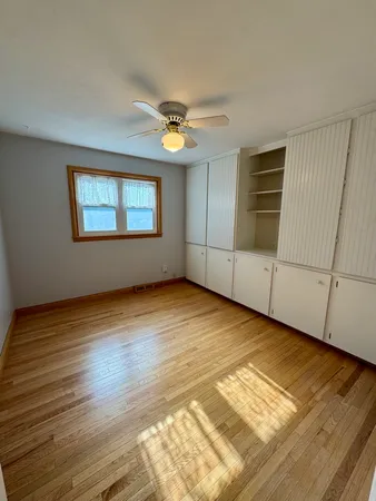 an empty room with wooden floor chandelier fan and windows