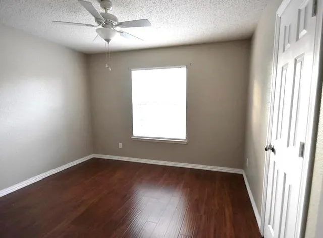 an empty room with wooden floor fan and windows