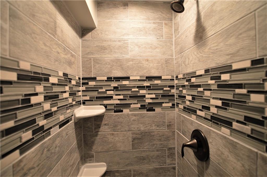 1947 Spring Valley Road Pittsburgh, PA 15243 - Photo 22 of 24 A view into the tiled shower in the basement bathroom. Three is 'wood look' porcelain tile on the walls, a decorative glass mosaic accent border, 2 soap/shampoo shelves and oil rubbed bronze fixtures and accessories.