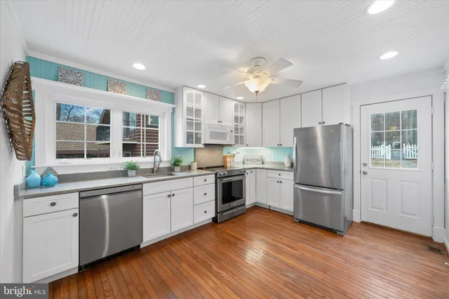 a kitchen with granite countertop a refrigerator a sink dishwasher a stove and white cabinets with wooden floor