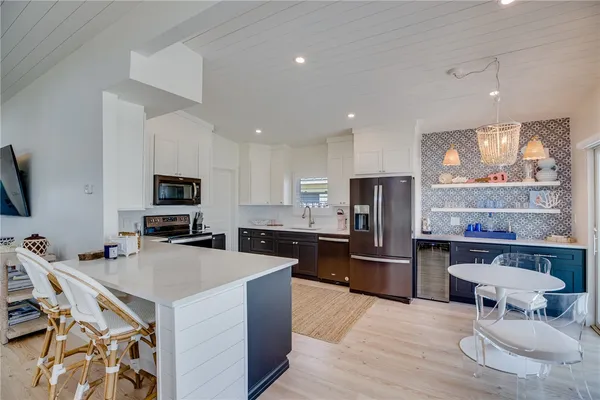 a kitchen with stainless steel appliances a microwave a stove a refrigerator a sink a dining table and chairs with wooden floor