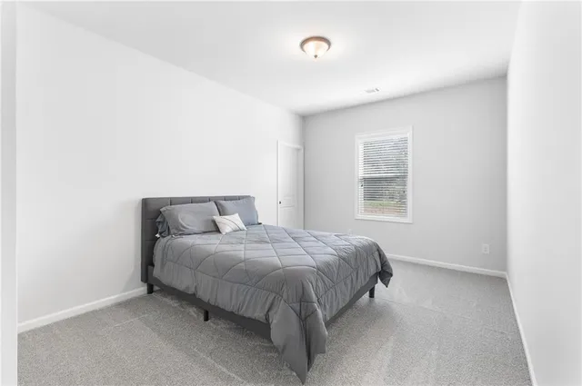 a bed sitting in a spacious bedroom next to a window and a lamp