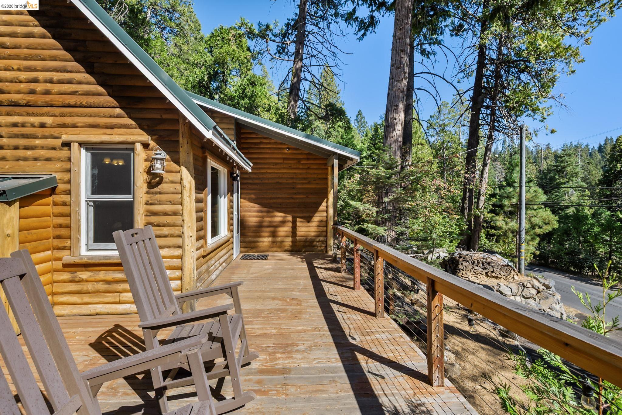 25972 Long Barn Road Long Barn, CA 95335 - Photo 25 of 36 Log cabin exterior with an expansive wooden deck, featuring a cable railing system and a wall-mounted exterior light fixture