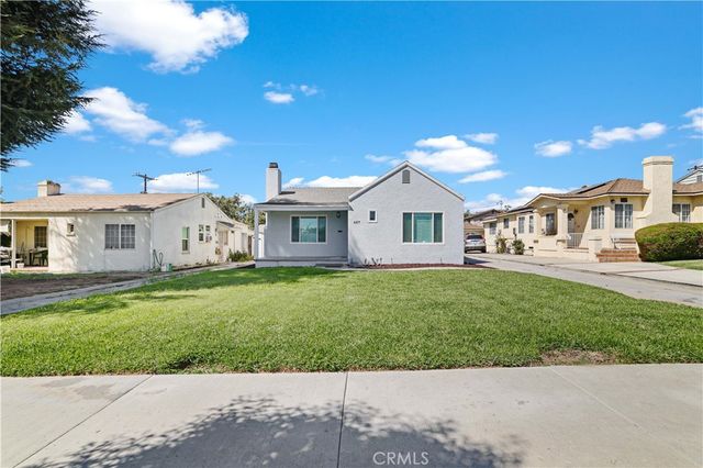 a view of a white house in front of a big yard with plants and large trees
