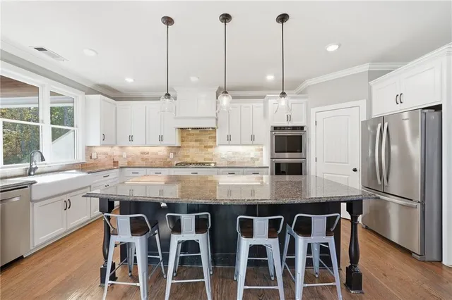 a kitchen with stainless steel appliances granite countertop a sink a stove a refrigerator and island with wooden floor