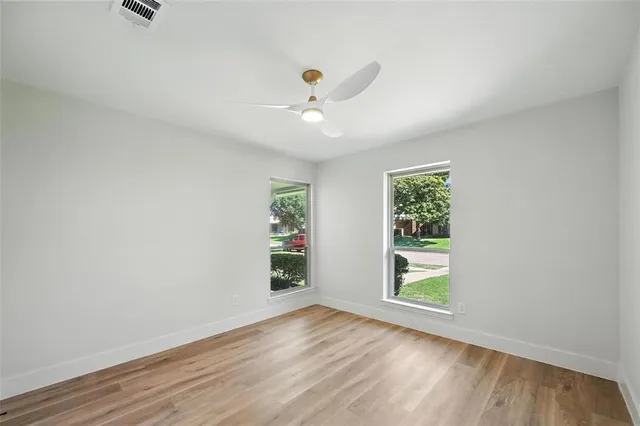 an empty room with wooden floor chandelier fan and windows