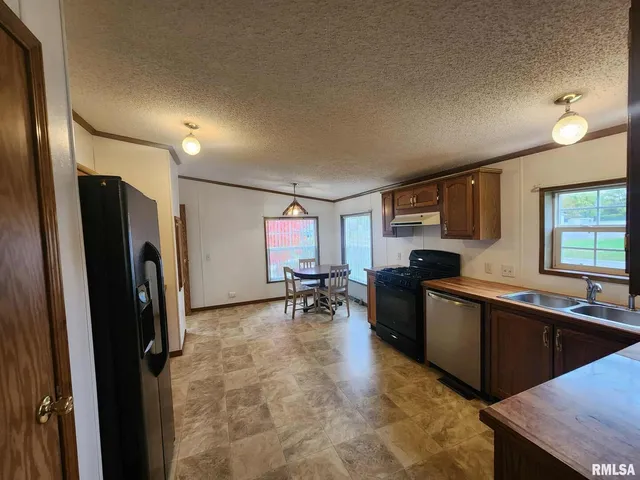 a kitchen with stainless steel appliances granite countertop a refrigerator a sink dishwasher a stove and a dining table with wooden floor