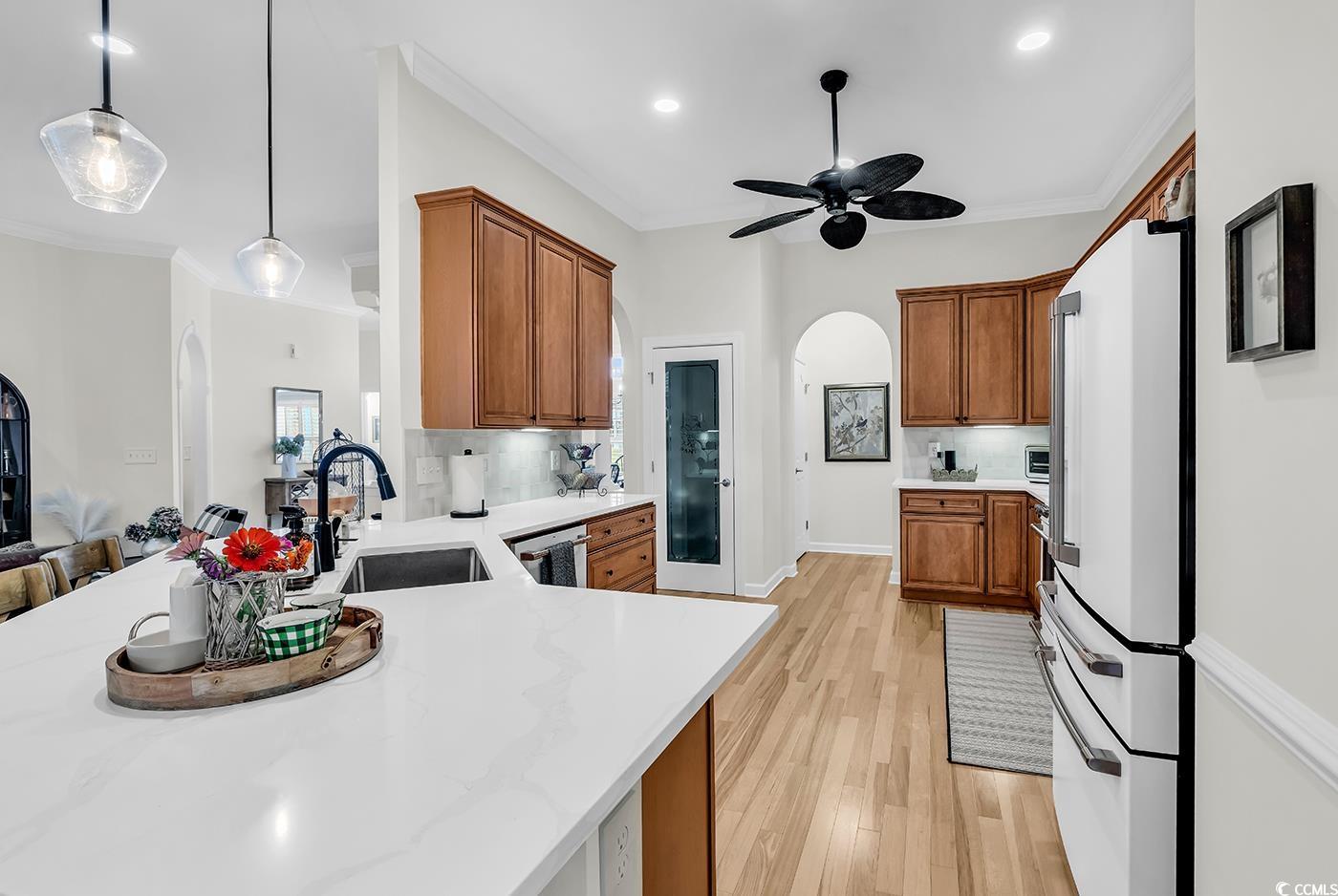 9 Saltwind Loop Murrells Inlet, SC 29576 - Photo 12 of 38 Kitchen with brown cabinetry, arched walkways, light wood-style flooring, crown molding, and hanging light fixtures