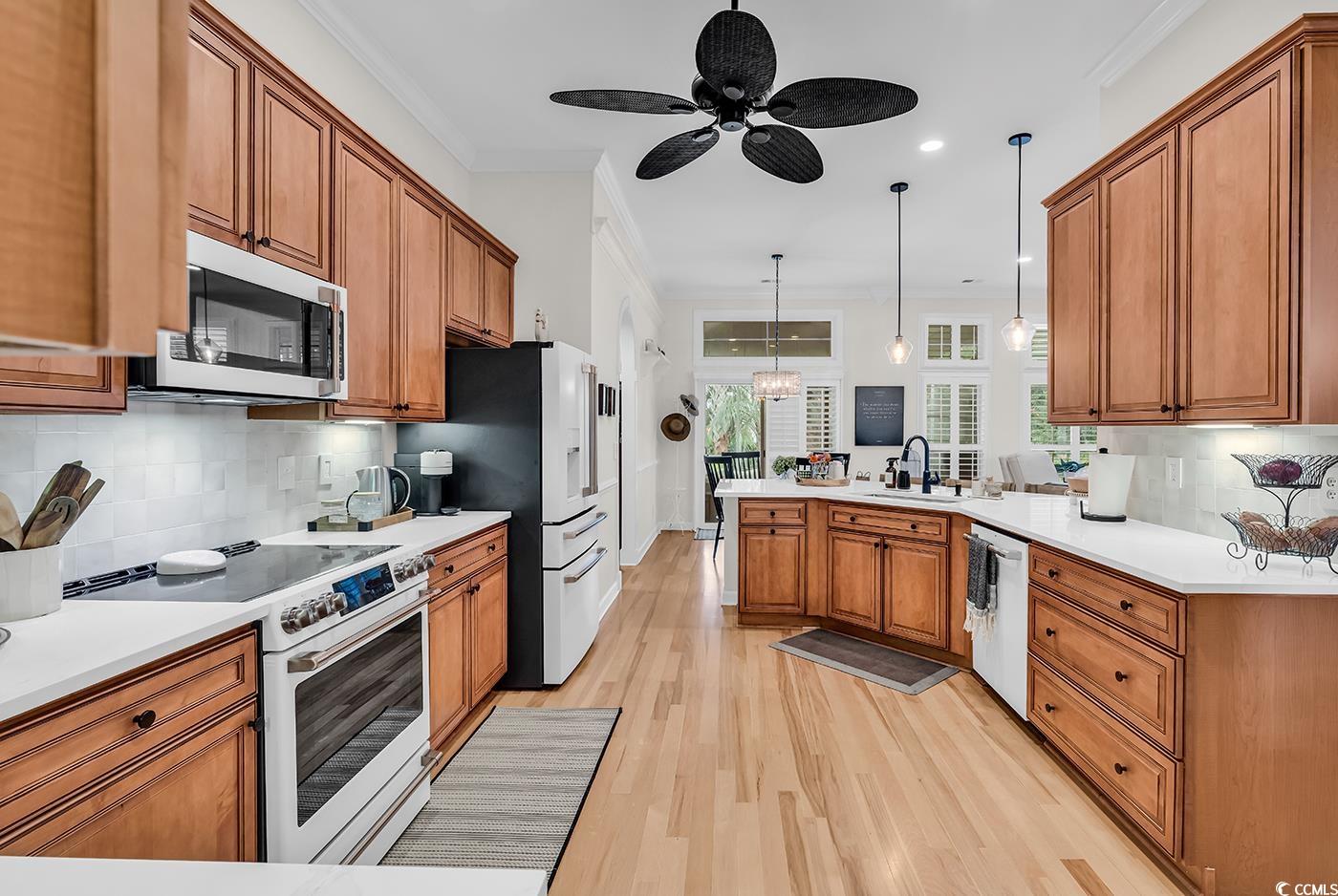 9 Saltwind Loop Murrells Inlet, SC 29576 - Photo 14 of 38 Kitchen with decorative backsplash, brown cabinetry, white appliances, crown molding, and a peninsula