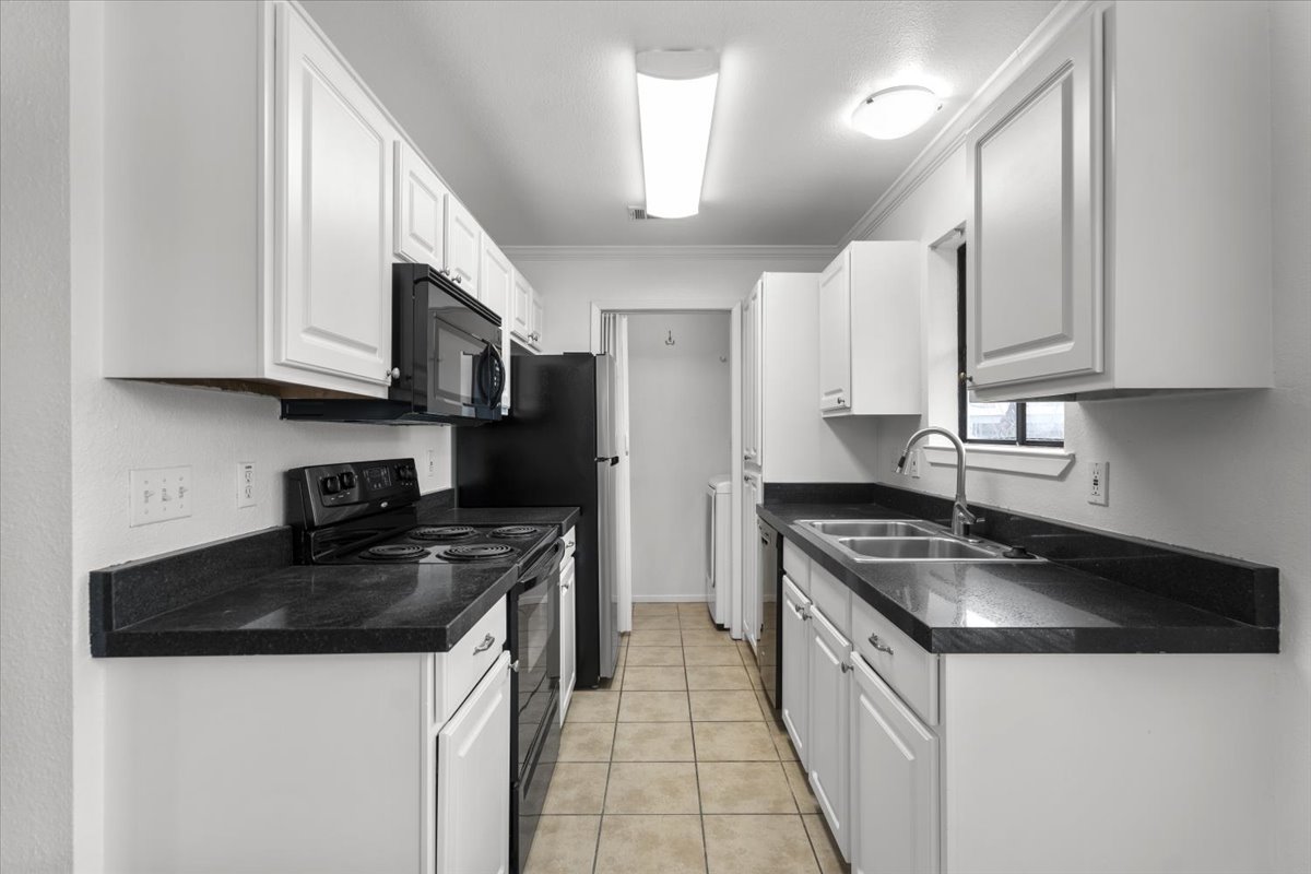 2018 West Rundberg Lane, Unit 9A Austin, TX 78758 - Photo 8 of 30 Kitchen featuring granite countertops, black electric range, microwave, updated cabinetry, light tile floors, dishwasher, and new refrigerator. Laundry room is center rear.