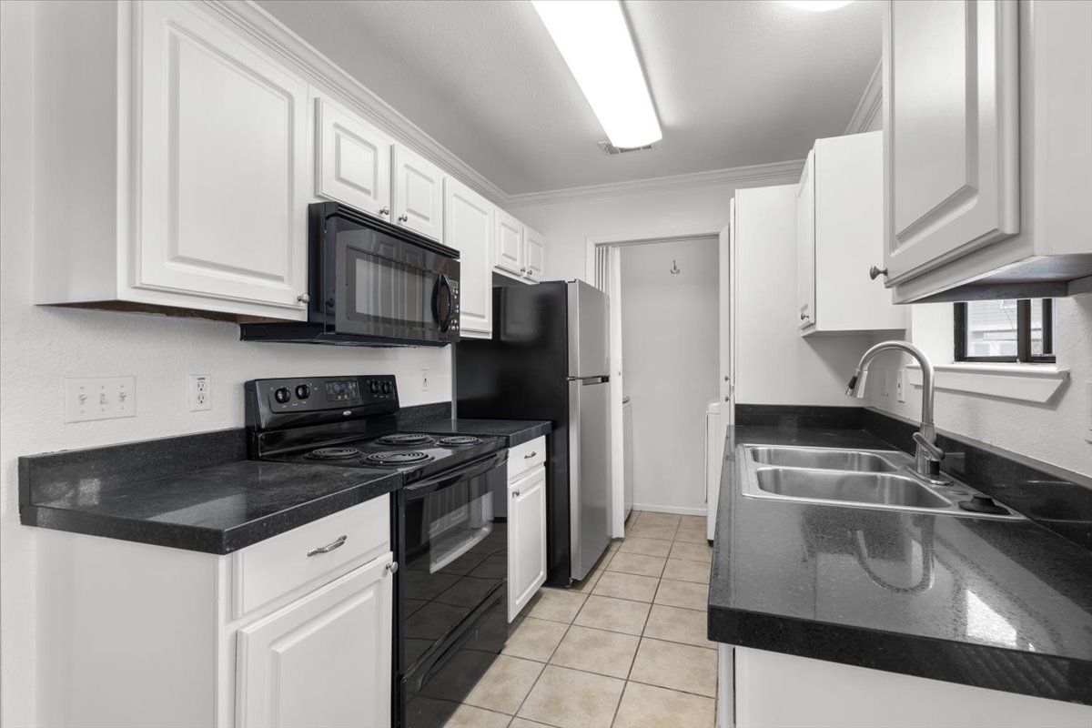 2018 West Rundberg Lane, Unit 9A Austin, TX 78758 - Photo 9 of 30 Kitchen featuring granite countertops, black electric range, microwave, updated cabinetry, light tile floors, dishwasher, and new refrigerator. Laundry room is center rear.