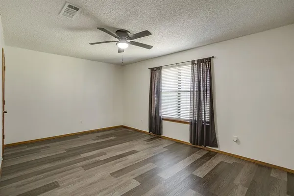 an empty room with wooden floor fan and windows