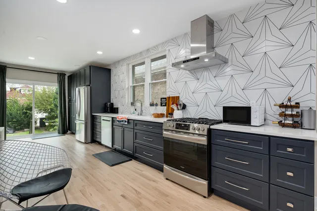 a kitchen with stainless steel appliances kitchen island granite countertop a stove a sink dishwasher and white cabinets with wooden floor