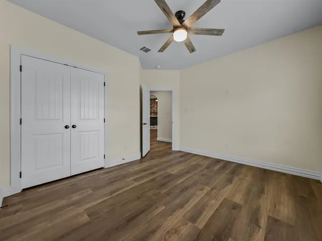 an empty room with wooden floor fan and windows