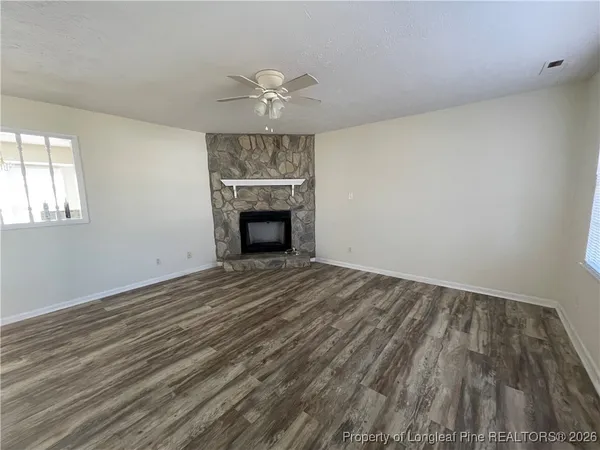an empty room with wooden floor fireplace and windows