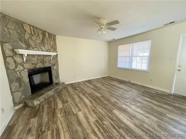 a view of an empty room with wooden floor fireplace and a window