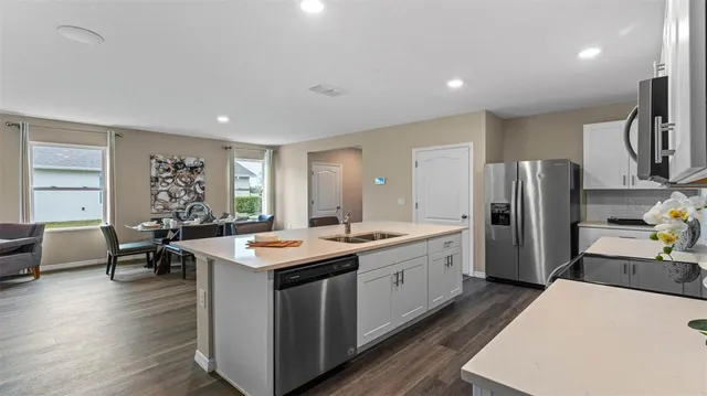 a kitchen with stainless steel appliances granite countertop a refrigerator a sink dishwasher a dining table and chairs with wooden floor