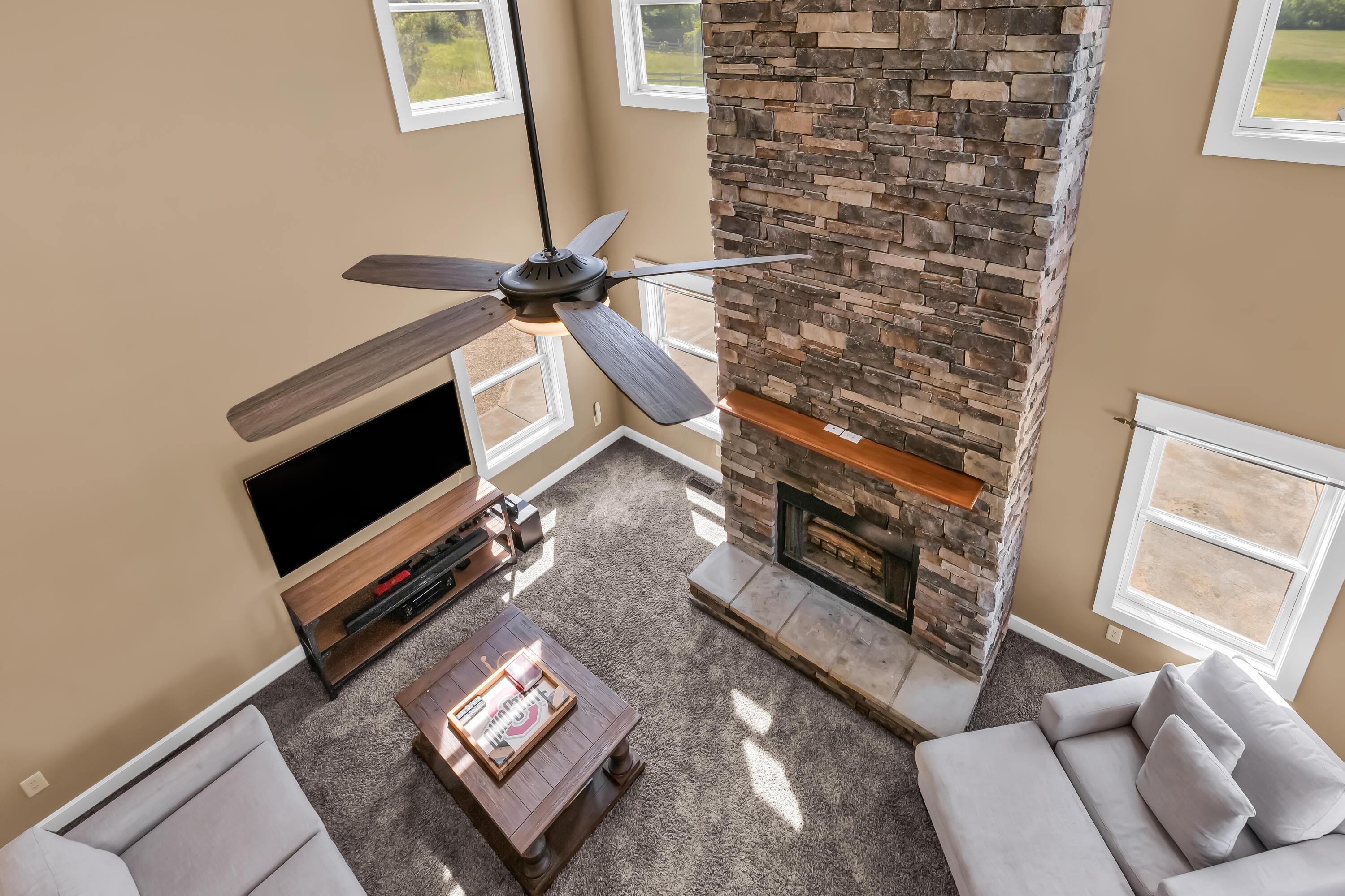 16689 Bailor Road Laurelville, OH 43135 - Photo 29 of 73 • Light sand carpet
• Tan painted walls
• Two story ceiling
• New lighted ceiling
fan ~ 2025
• Stone floor to ceiling,
woodburning fireplace
with raised hearth &
mantle