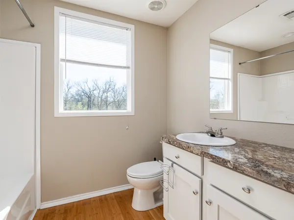 a bathroom with a granite countertop toilet a sink and a window