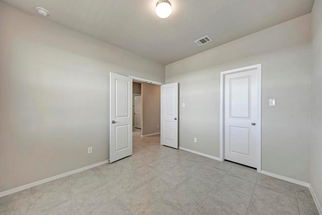 1209 Goforth Road Kyle, TX 78640 - Photo 21 of 32 A well-lit bedroom features cool-toned tile flooring and bright white doors, creating a serene and adaptable living space.