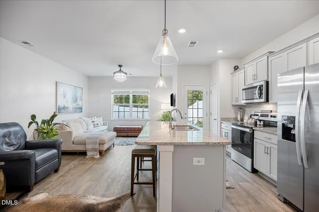 a kitchen with stainless steel appliances granite countertop a refrigerator a sink dishwasher a stove and white cabinets with wooden floor