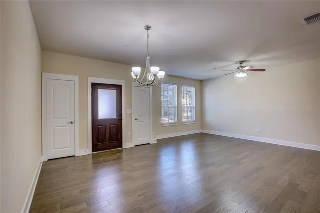 a view of an empty room with wooden floor and chandelier