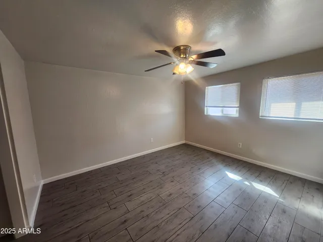 an empty room with wooden floor fan and windows