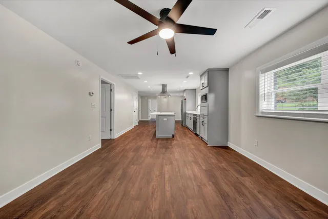 a big room with wooden floor a chandelier fan and windows