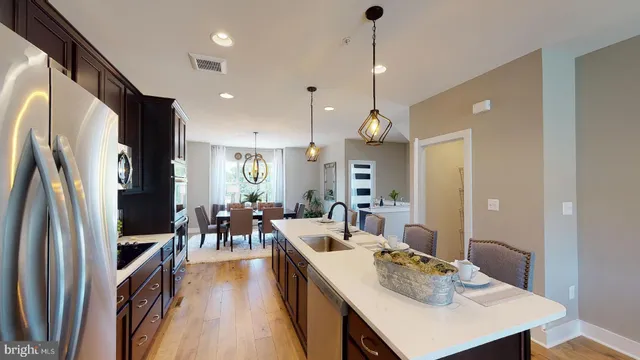 a kitchen with stainless steel appliances granite countertop a refrigerator a sink dishwasher a dining table and chairs with wooden floor