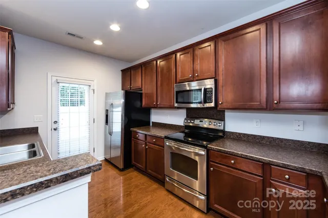 a kitchen with stainless steel appliances granite countertop a refrigerator a sink dishwasher a oven and a dining table with wooden floor