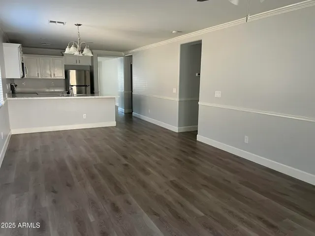 an empty room with wooden floor kitchen view and a chandelier