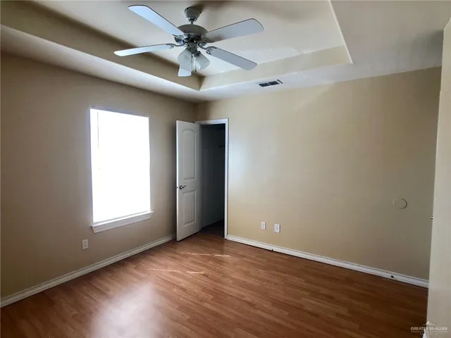 an empty room with wooden floor chandelier fan and windows