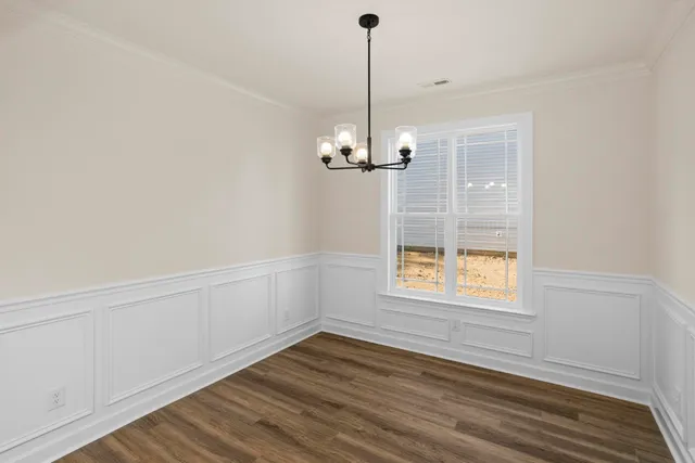 a view of an empty room with wooden floor kitchen view and a window
